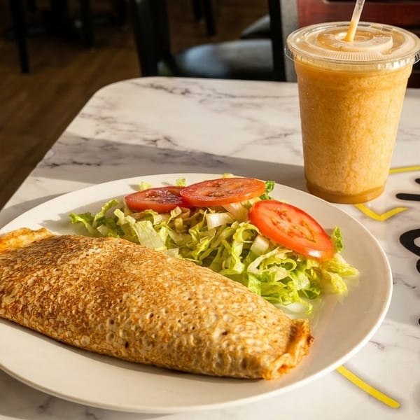 A golden savory crepe, fresh salad, and orange smoothie on a marble table.