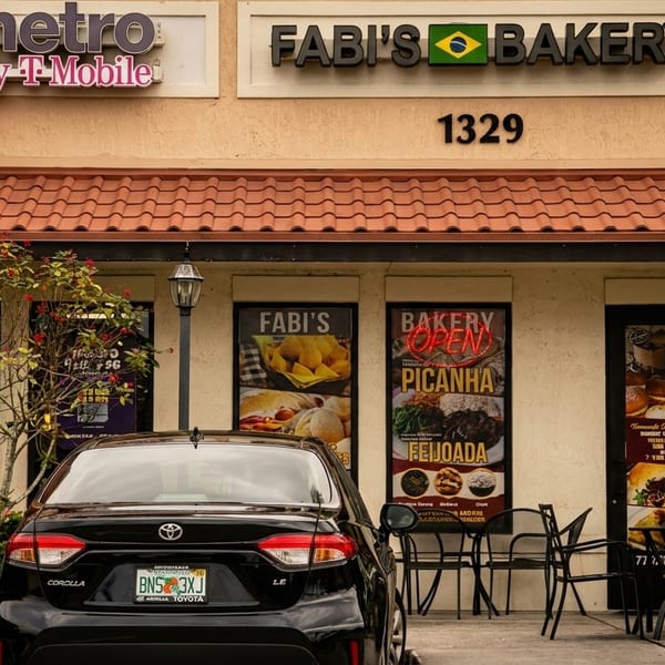 Fabi's Bakery storefront with Brazilian food displays, outdoor seating, and a black car.