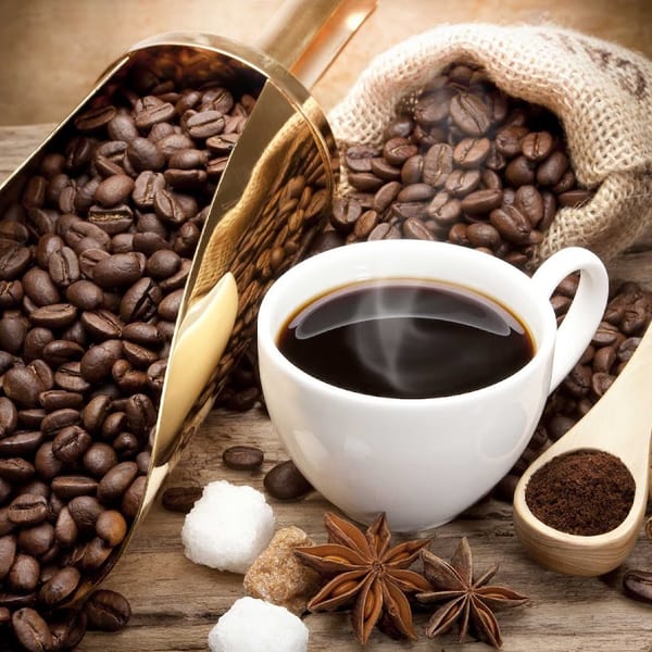 Steaming cup of coffee with beans, sugar cubes, star anise, and cinnamon sticks on wood.
